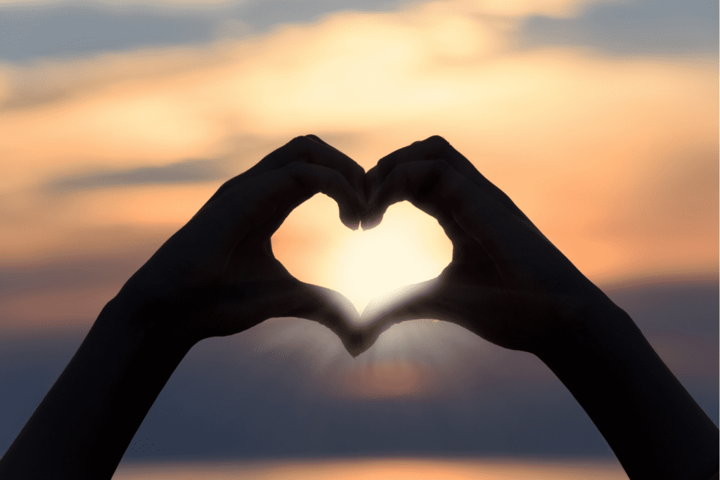 Photo of two hands making a heart in front of a beautiful sunset